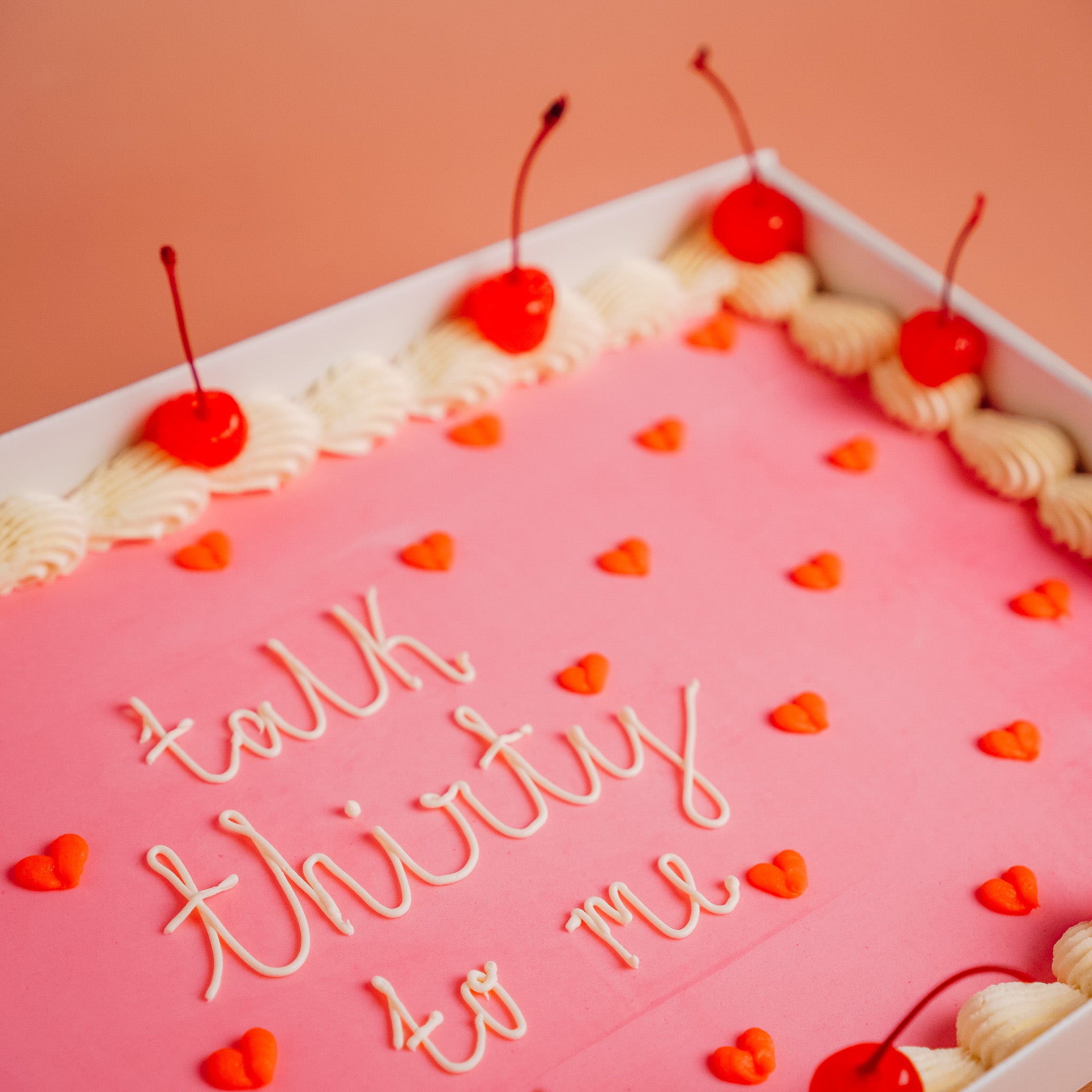 close up of a sheet party cake with. a personalized piped message on top in white. the cake is pink and orange