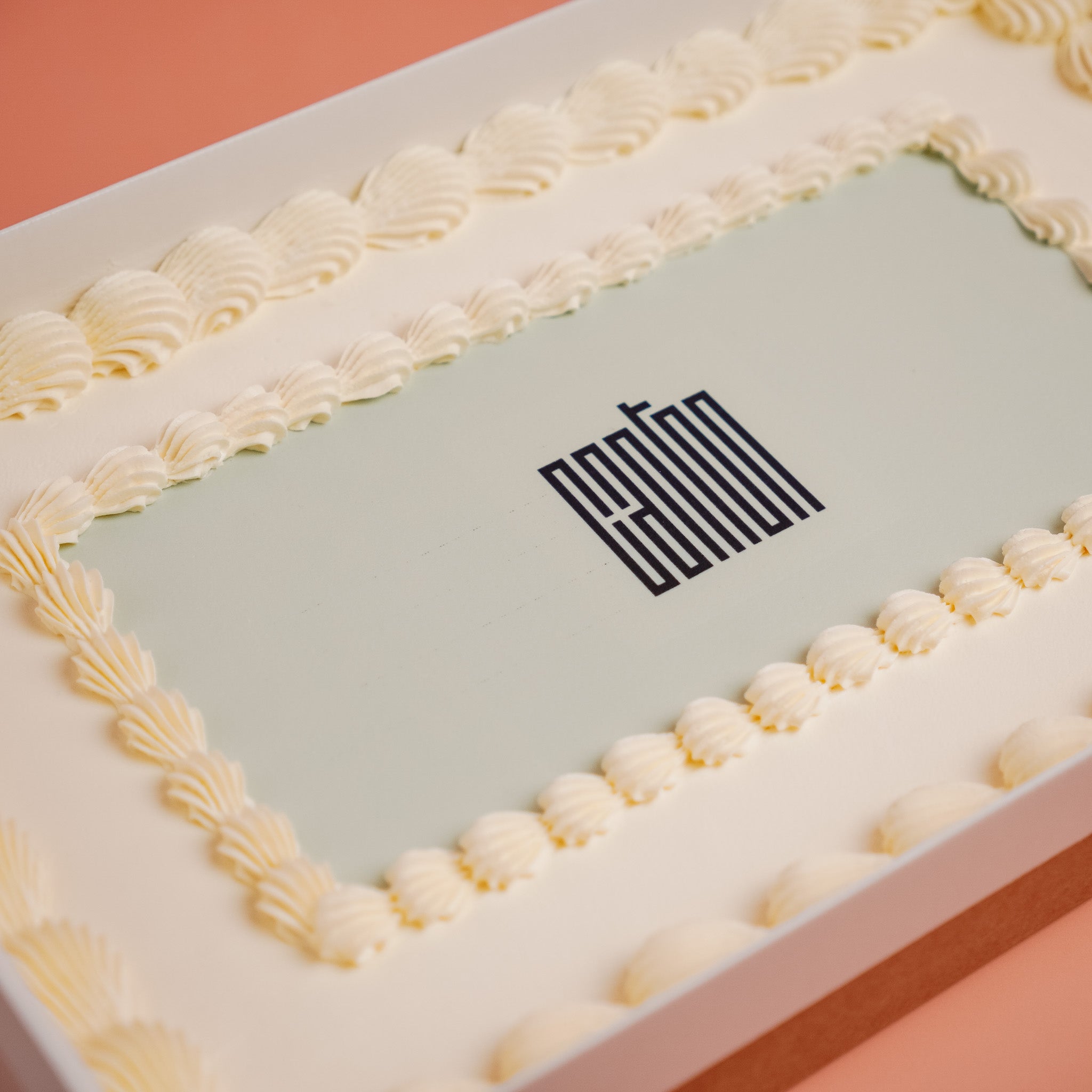 Rectangular cake with white frosting and a brand logo on a pink background