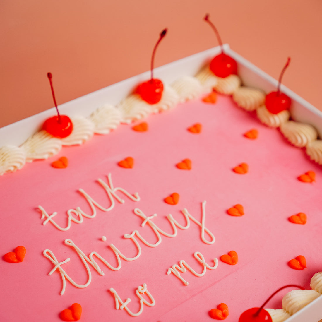 close up of a sheet party cake with. a personalized piped message on top in white. the cake is pink and orange