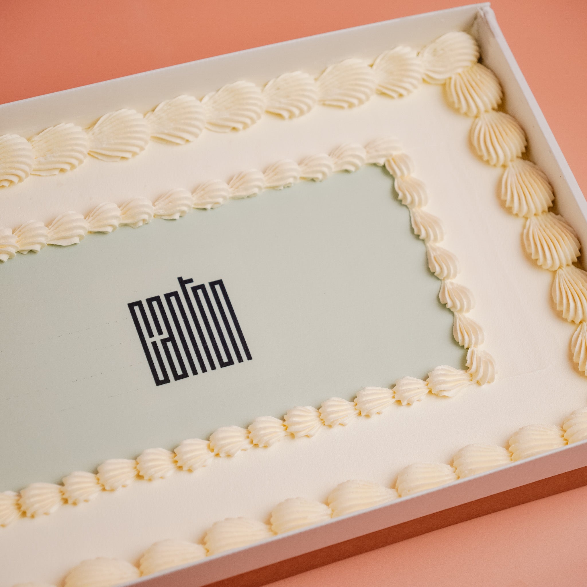 Rectangular cake with decorative white icing with a compant logo on a pink background