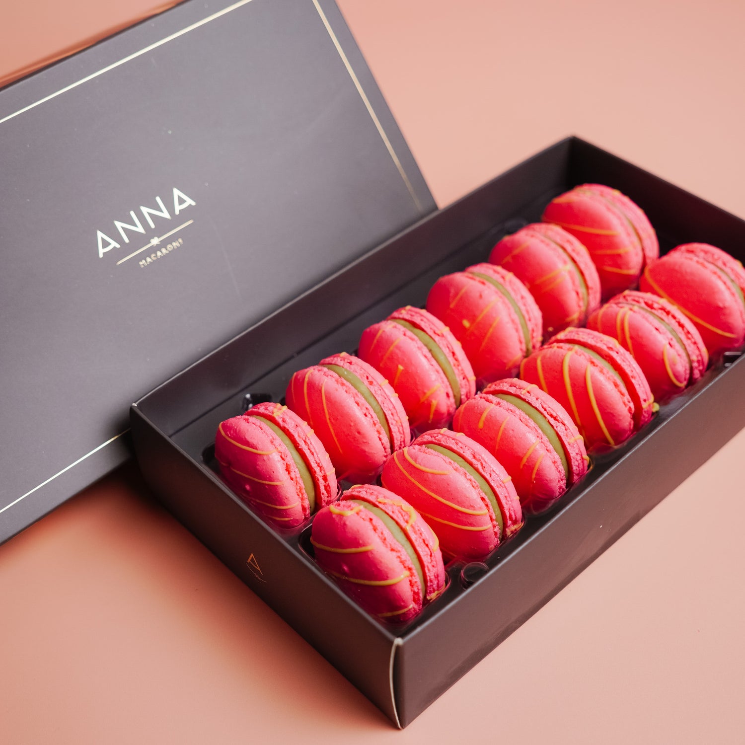 Box of pink &amp; green matcha macarons with gold accents on a pink background, featuring the brand &