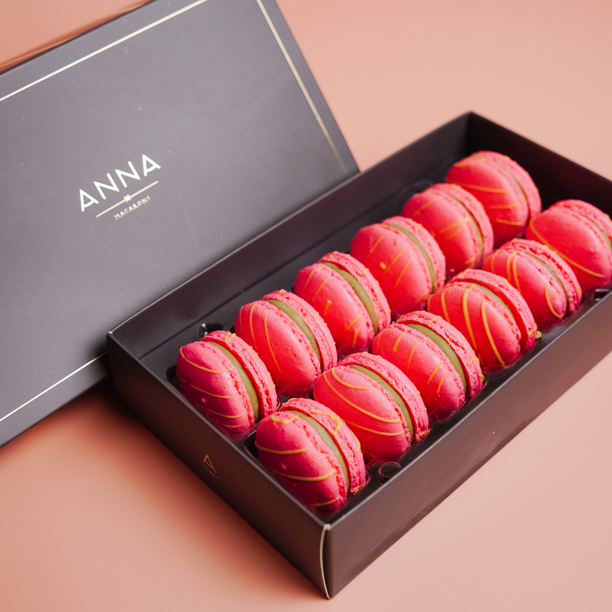 Box of pink &amp; green matcha macarons with gold accents on a pink background, featuring the brand &