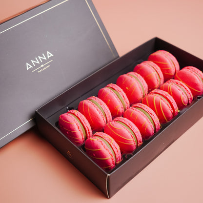 Box of pink &amp; green matcha macarons with gold accents on a pink background, featuring the brand &