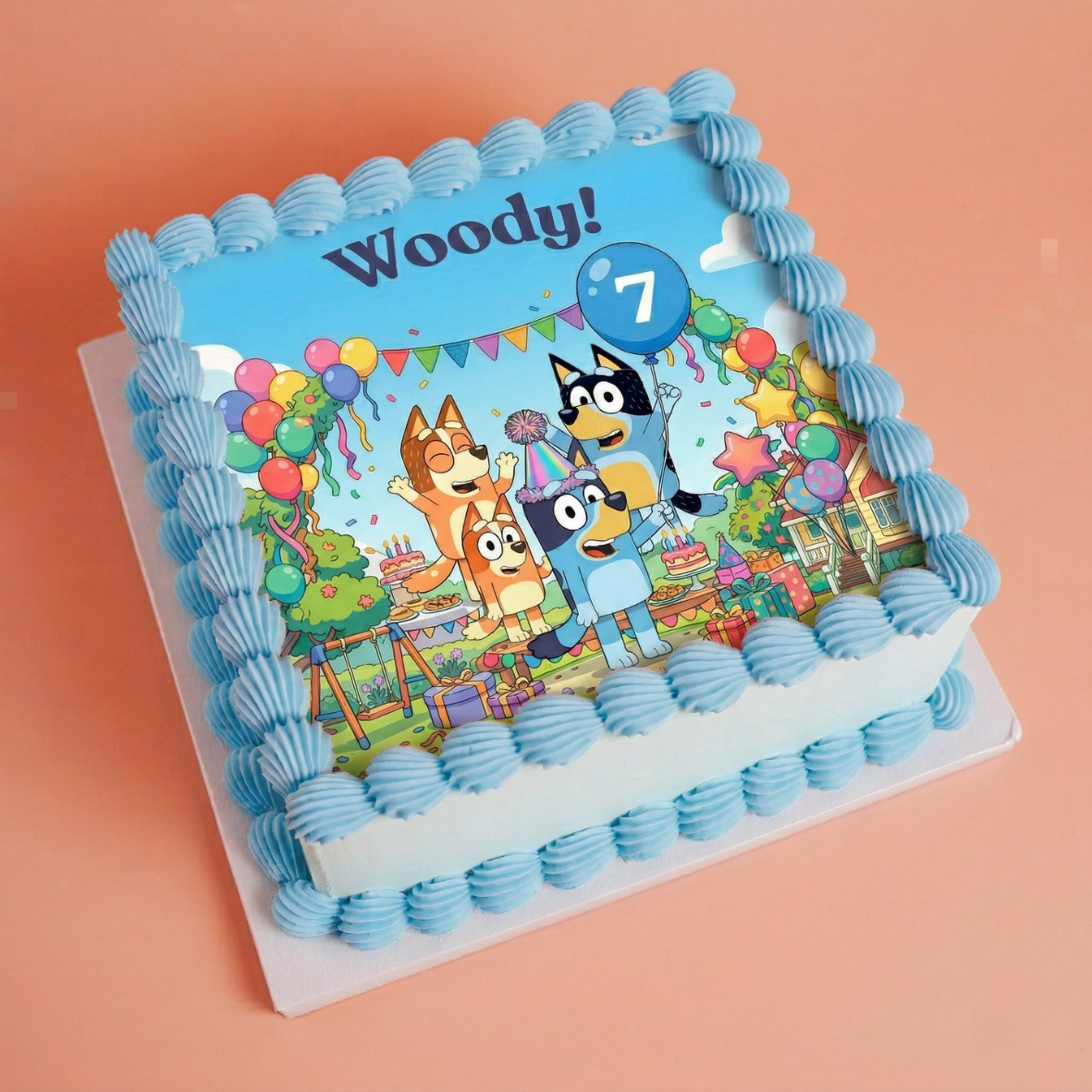 Blue bluey cake, from the australian themed show, a sqaure vanilla cake with printed topper and blue buttercream shells photographed on a peach backgrounf